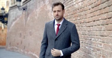 Zarif, uzun ceketli, mutlu genç bir adam. Ortaçağ şehrinin dışında kravat takarken başka tarafa bakıyor, gülümsüyor.