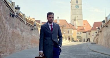 Havalı bir iş adamı bir evrak çantası ve bir el cepte, açık havada yürüyor.