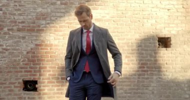 Çekici iş adamı ceketini düzeltiyor, kameraya bakıyor ve duvara gülümsüyor.