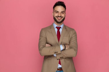 Çekici iş adamı kameraya gülümsüyor ve kollarını pembe arka planda kavuşturuyor.