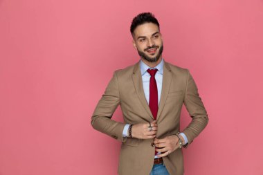 Çekici iş adamı ceketini ayarlıyor ve pembe arka planda bir gülümsemeyle yüzünü çeviriyor.