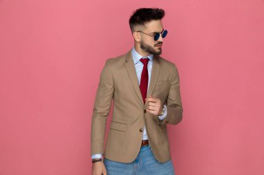 Çekici bir iş adamı pembe arka planda poz verirken sert bir tutum sergiliyor.