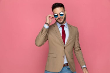 Genç yakışıklı iş adamı güneş gözlüğünü takıyor ve pembe arka plana karşı tavır takınıyor.