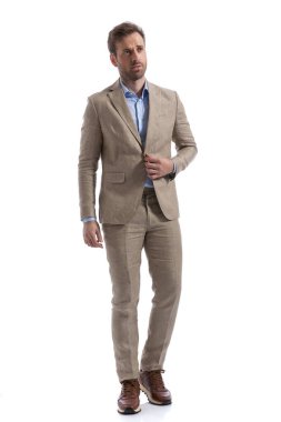 Genç işadamı ceketinin düğmelerini açıyor, başka tarafa bakıyor ve beyaz arka plana karşı poz veriyor.