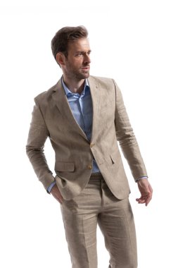 Seksi iş adamı gözünü kaçırıyor, bir eli cebinde ve beyaz arka planda poz veriyor.