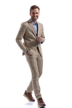 Kameraya bakıp bir elini cebinde tutarken kenarda yürüyen mutlu bir işadamı. 