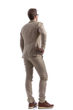Bir eli kalçasında duran ve bir şeyler düşünen yakışıklı bir iş adamının arkadan görünüşü.