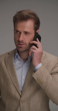 Takım elbiseli kendine güvenen bir işadamı telefonda konuşuyor, beni işaret ediyor ve beni arıyor ve gri arka planda bir jest yapıyor.