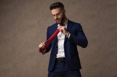 Kaba tavırlı, kravatını düzelten, duvar kağıdına karşı gözlük takan manken.