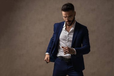 Güçlü mevcudiyeti olan seksi iş adamı ceketini çıkarıp duvar kağıdına poz veriyor.