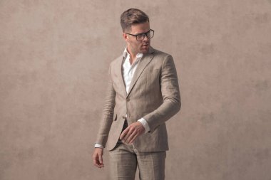 Takım elbiseli çekici bir genç adam. Gözlüklü, kendine güvenen poz veren ve Studi 'de bej arka planda duran.