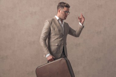 Çekici iş adamının bavulu tutuşu, el hareketi yapması ve stüdyoda bej arka planda yürümesi.