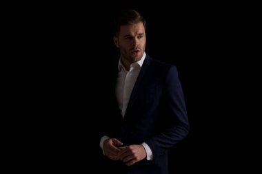 Stüdyoda siyah arka planda modada dikilirken konuşan ve parmaklarına dokunan takım elbiseli gizemli genç adam.