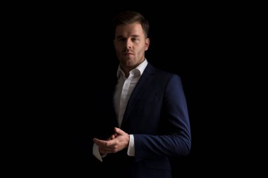 Stüdyoda siyah arka planda poz verirken mavi takım elbiseli ve avuçlarına dokunan havalı genç adamın dramatik portresi.