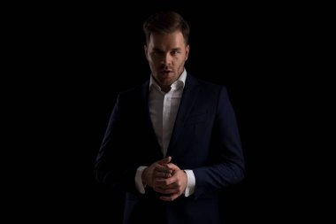 Lacivert takımlı çekici bir moda adamının portresi avuçlarını ovuyor ve stüdyoda siyah arka planda poz veriyor.
