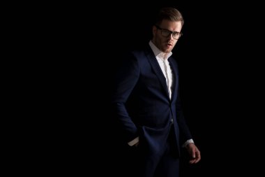 Takım elbiseli, gözlüklü seksi genç adamın yan görünüşü. El ele tutuşup stüdyoda siyah arka planda poz veriyor.