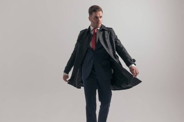 Takım elbiseli, uzun paltolu çekici ve zarif bir adam. Stüdyoda gri arka planda yürüyordu.