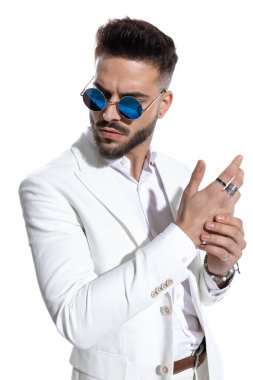 Eski güneş gözlüklü havalı sakallı adam avuçlarını beyaz arka planda gezdirirken başka yöne bakıyor ve poz veriyor.