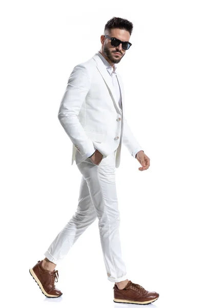 ポケットにサングラスをかけスタジオで白地を背景にファッションライトを歩くクールなビジネスマンの側面図 — ストック写真