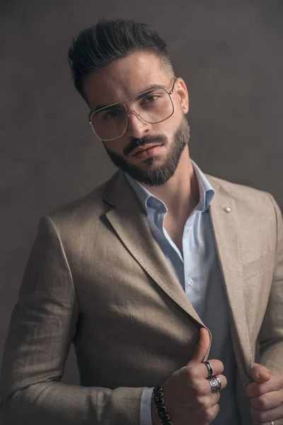 Sexy Businessman Beige Suit Eyeglasses Pulling Jacket Posing Front Brown — стоковое фото