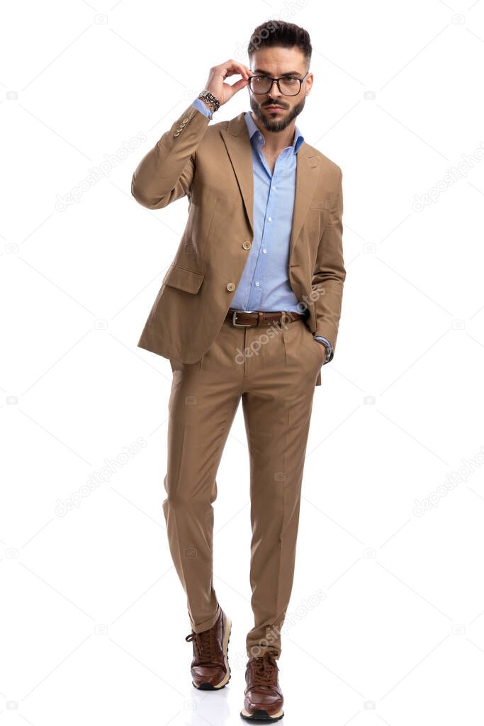 full body picture of sexy businessman looking away and fixing glasses while walking isolated on white background in studio