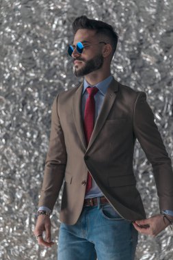 Güneş gözlüklü, gümüş folyo arka planda poz veren, tıraşsız yakışıklı bir adamın portresi.