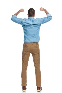 Heyecanlı genç adamın havaya yumruk atması ve stüdyodaki beyaz arka planda zaferi kutlaması.