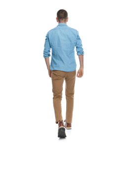 Chino pantolonlu ve spor ayakkabılı sıradan bir genç stüdyoda beyaz arka planda yürüyor ve poz veriyor.