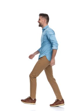 Chino pantolonlu sıradan bir sakallı adam. Stüdyoda beyaz arka planda tek başına yürürken yan bakıp gülümsüyor.
