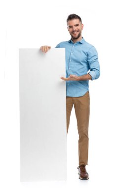 Kot tişörtlü, elinde boş tahtayla gezen, gülümseyen ve beyaz arka plandaki çalışmalarına güvenen gururlu bir adamın tüm vücudu.