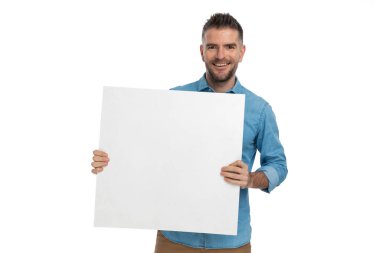 Tıraş olmamış gururlu bir adam tahtayı tutuyor ve gülümserken reklamını yapıyor ve beyaz arka plandaki işine güveniyor.