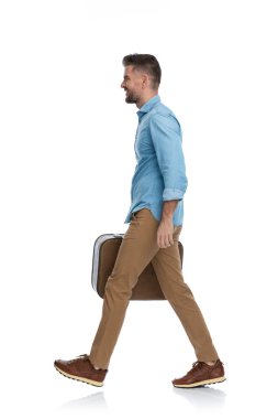 Dünya turu için havaalanına giden genç bir adamın yan görüntüsü. Şehirden ayrılıp tatilin tadını çıkarıyor, beyaz arka planda yürüyor.