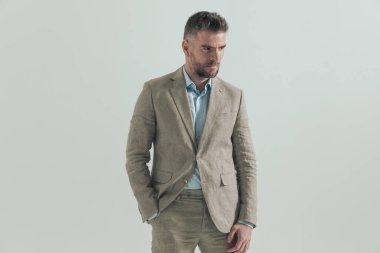 Çekici, orta yaşlı, el ele tutuşmuş ve gri arka planda kendine güvenen bir duruş sergileyen bir adam. 