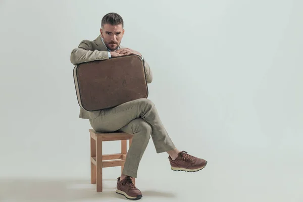 Nieogolony Młody Człowiek Garniturze Bagażem Siedzący Drewnianym Krześle Opuszczający Miasto — Zdjęcie stockowe