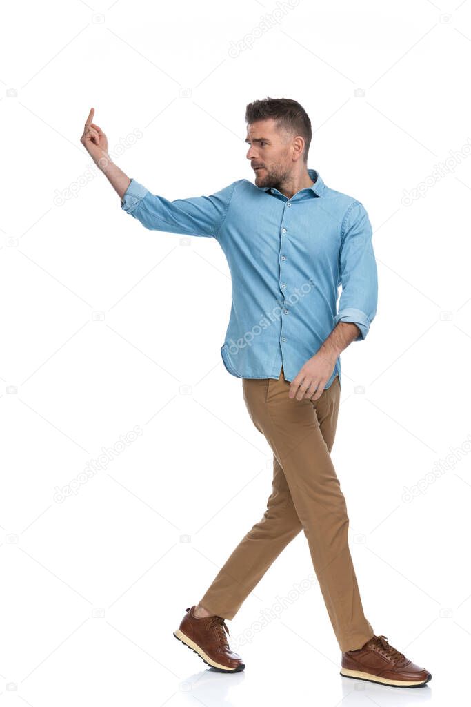 upset casual guy on white background wearing blue denim shirt and chino pants with sneackers looking over shoulder and showing middle finger