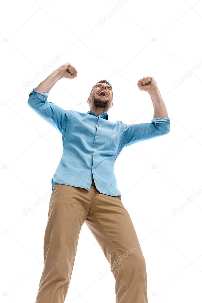 low angle view surprising enthusiastic young guy with arms in the air, enjoying the victory and laughing on white background