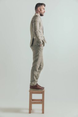 Sakallı, el ele tutuşan ve tahta sandalyede dikilen seksi iş adamının yan görüntüsü.