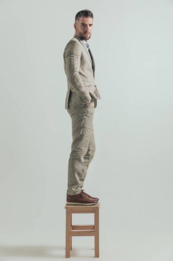 Tahta sandalyede elleri ceplerinde duran sakallı genç işadamının yan görünüşü ve rahat bölgesinden çıkmayı düşünmesi.