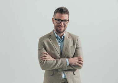 Gözlüklü, yakalı, kollarını kavuşturup gri arka planda gülümseyen mutlu bir iş adamı.