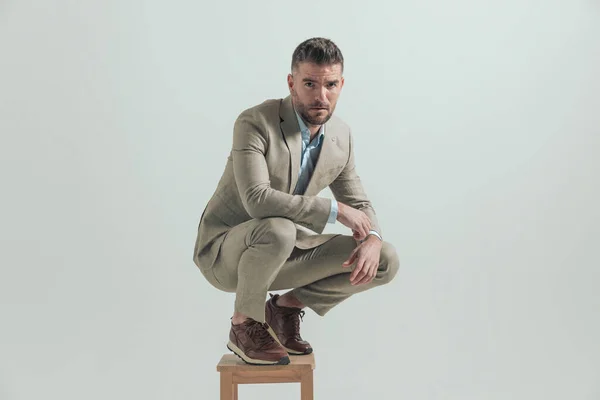 在演播室里 四十多岁的有魅力的男人双膝肘弯 蹲在灰色背景的木椅上 — 图库照片