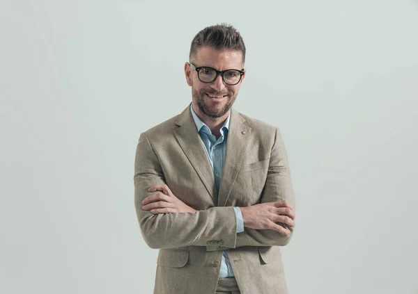 happy businessman with glasses and open collar shirt folding arms and smiling on grey background