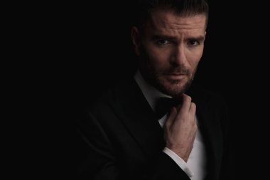 Siyah arka planda siyah smokinli yakışıklı iş adamı papyon takıyor ve kendine güvenerek poz veriyor.