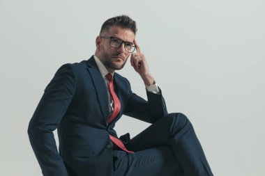 Kırklı yaşlardaki şık takım elbiseli bir işadamı parmak uçlarına basıyor ve stüdyoda gri arkaplan önünde düşünmeye teşvik ediyor.