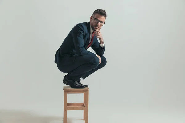 膝の上で肘を保持スーツの思慮深いビジネスマンや考えながら 灰色の背景にスタジオで木製の椅子に座って — ストック写真