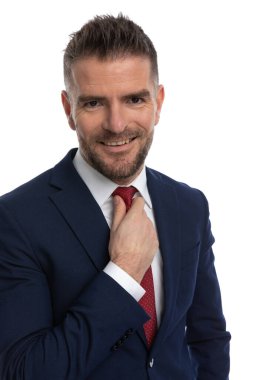 Lacivert takım elbiseli yakışıklı bir adamın portresi. Gülümsüyor ve stüdyoda beyaz arka planda kırmızı kravat takıyor.