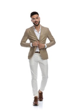 Akıllı, sıradan bir adam ceketinin düğmelerini açıyor, kameraya doğru yürüyor ve beyaz arka plana bakıyor.