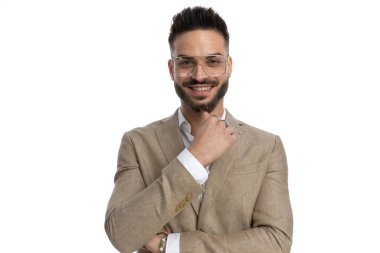 Yakışıklı iş adamı kameraya gülümsüyor, kollarını kavuşturup beyaz arka planda çenesine dokunuyor.