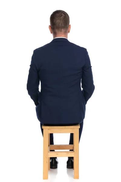 在演播室里 一个优雅的灰蒙蒙男子坐在白色背景前的木椅上 — 图库照片