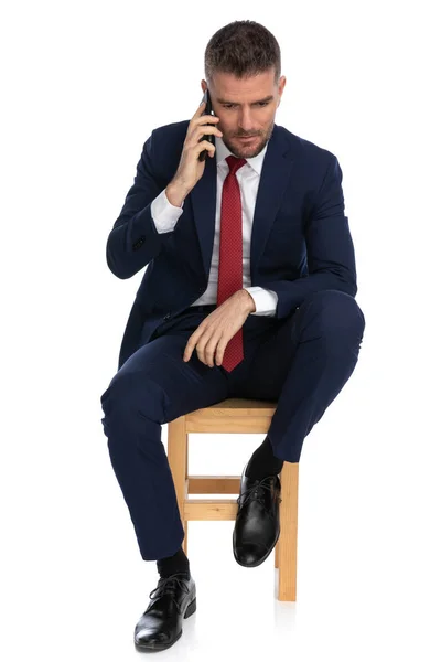 Elegancki Nieogolony Biznesmen Łokciem Kolanie Rozmawiający Przez Telefon Siedząc Drewnianym — Zdjęcie stockowe