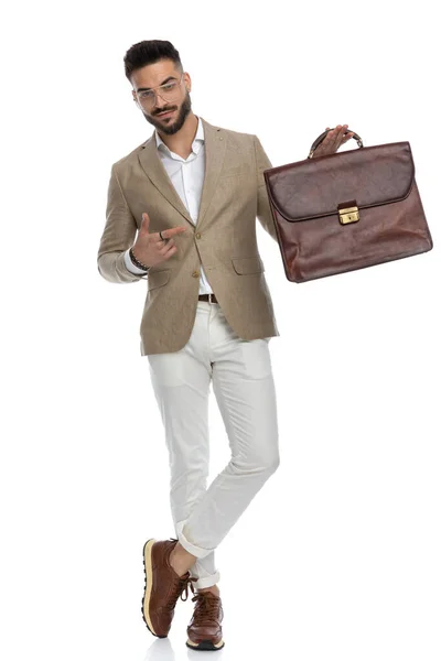 Привабливий Бізнесмен Вказуючи Свій Портфель Перетинаючи Ноги Посміхаючись Камеру — стокове фото